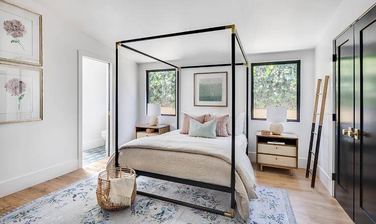 Bedroom features a CB2 frame canopy bed with pink and blue pillows atop a vintage rug and two-toned nightstands lit by alabaster lamps.