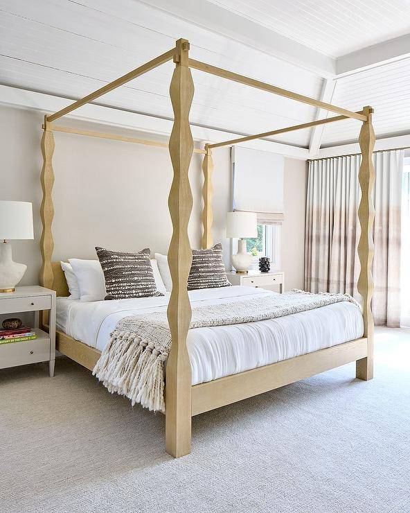 gold carved wood canopy bed with brown woven pillows flanked by white wooden nightstands and white and gold lamps.